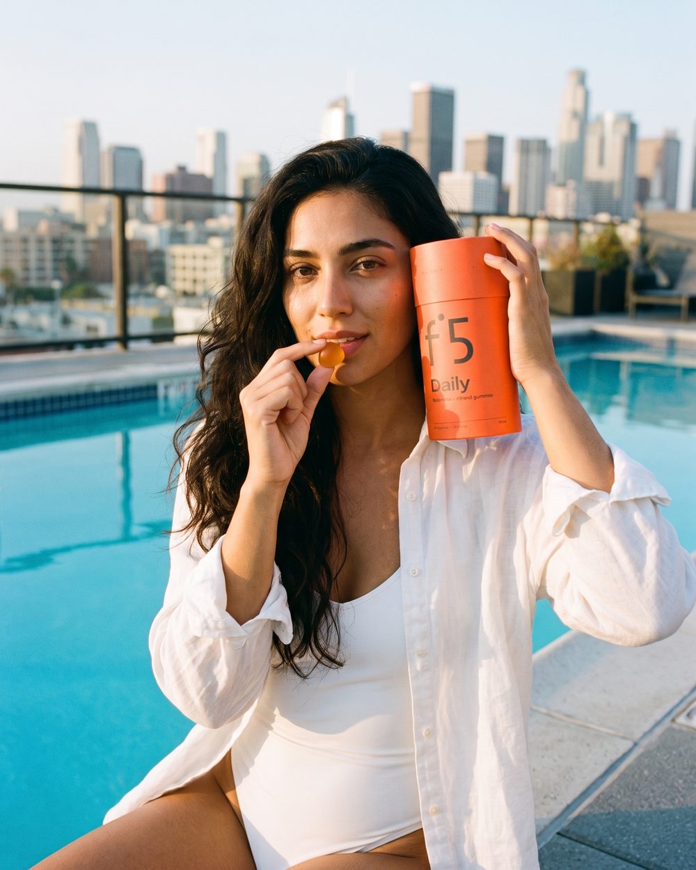 Young woman eating an f°5 gummy by a rooftop pool