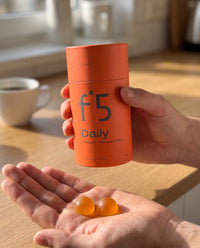Hand holding the f°5 Daily tube, two gummies in the other palm