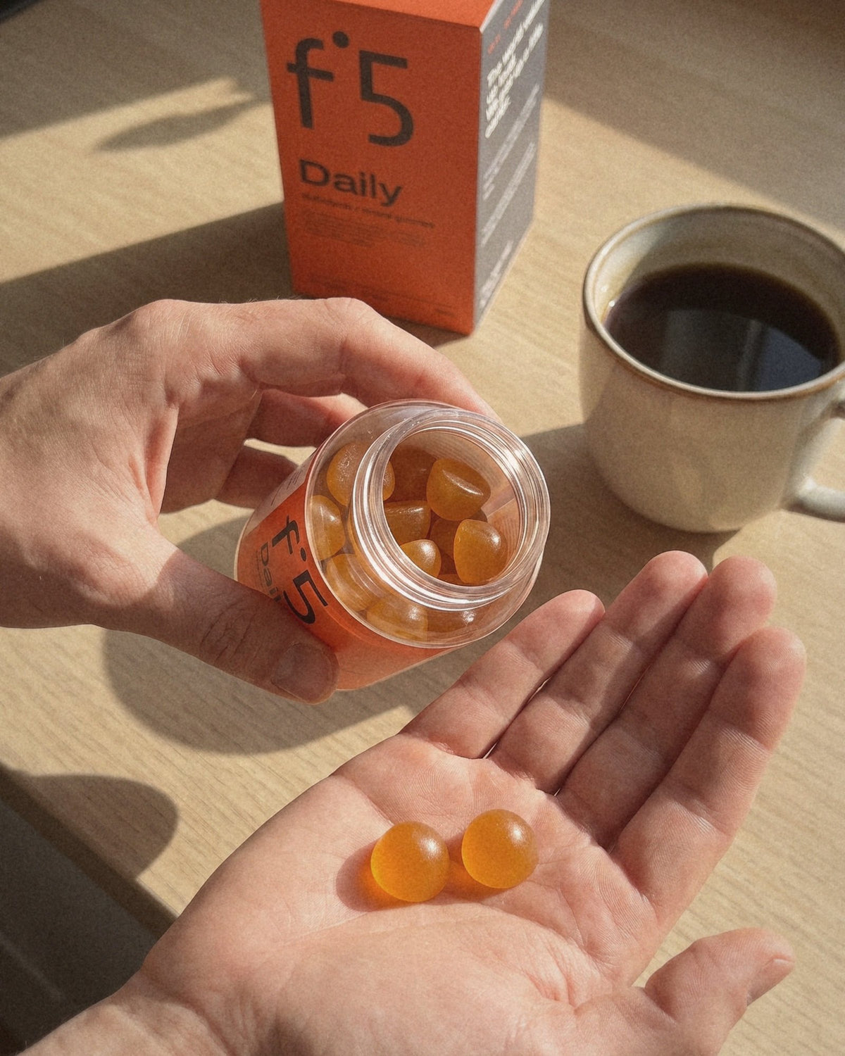 Two f°5 Daily gummies in a palm next to the open jar