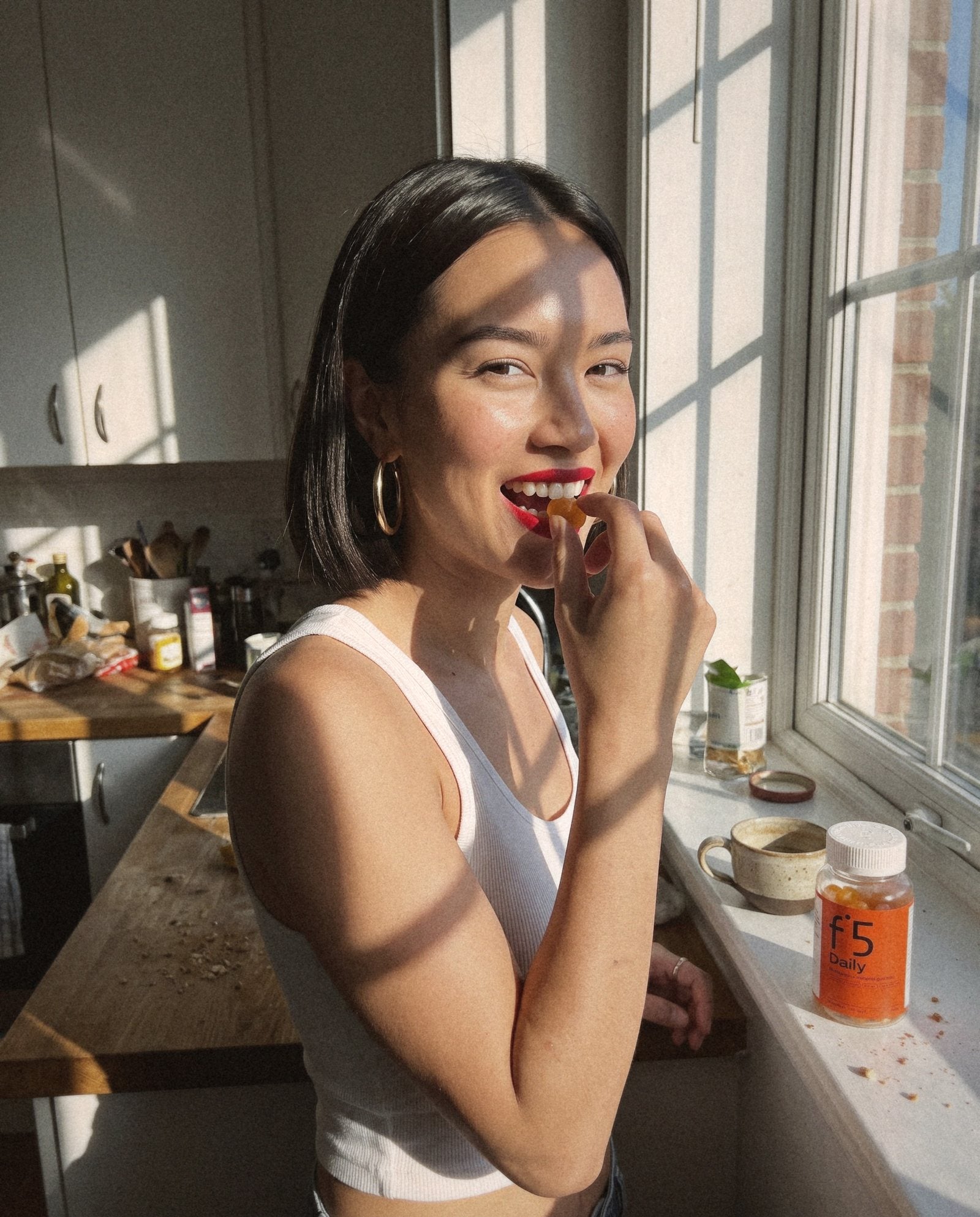 Young woman eating an f°5 Daily gummy by a sunny kitchen window